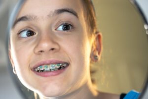Preteen girl with colorful braces smiling while looking at herself in the mirror during an orthodontic checkup
