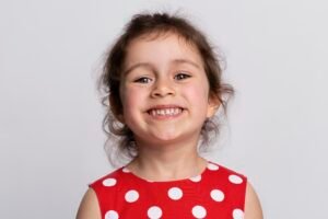 Smiling young girl in a red dress at an orthodontic visit, showing braces with baby teeth.